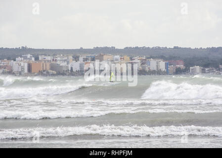 PALMA DE MALLORCA, SPAIN - FEBRUARY 2, 2019: Surfers ride big waves in the bay on a stormy gray afternoon on February 2, 2019 i Palma de Mallorca, Spa Stock Photo