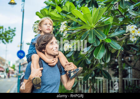 Dad and son sniffing group of yellow white flowers Frangipani, Plumeria on a sunny day with natural background Stock Photo