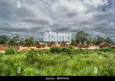 View of traditional village, thatched houses with roof and terracotta brick walls, cloudy sky as background, in Angola Stock Photo