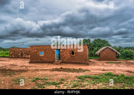 View of traditional village, thatched houses with roof and terracotta brick walls, cloudy sky as background, in Angola Stock Photo