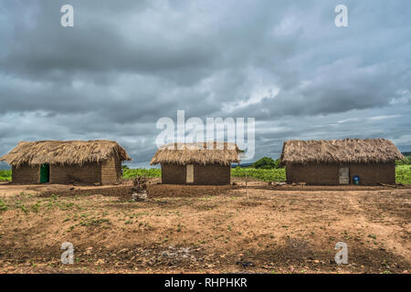 View of traditional village, thatched houses with roof and terracotta brick walls, cloudy sky as background, in Angola Stock Photo