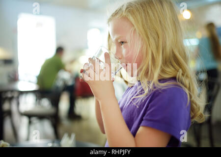 Cute little girl drinking water on hot summer day. Child holding a glass of water. Stock Photo