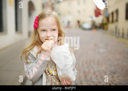 Adorable little girl eating fresh baked cookies on warm and sunny summer day in Vilnius, Lithuania Stock Photo