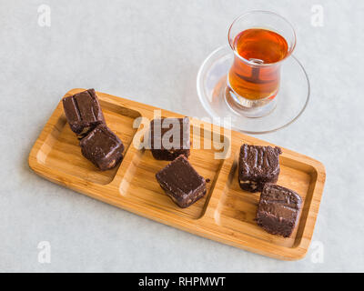 Chocolate cake cut into squares and served on a board with Turkish tea in a tea glass. Stock Photo
