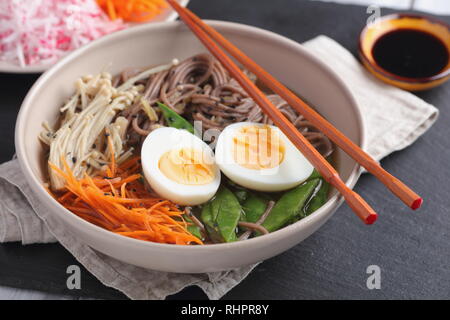 Japanese soup with Enoki mushrooms, soba noodles, boiled egg, carrot, radish, green beans, and soy sauce Stock Photo