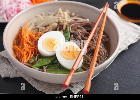 Japanese soup with Enoki mushrooms, soba noodles, boiled egg, carrot, radish, green beans, and soy sauce Stock Photo