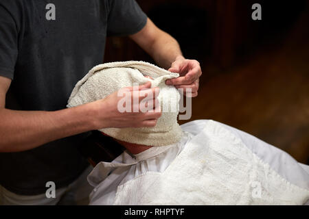 Client with hot towel on face before shaving in barber shop Stock Photo