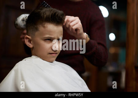 Children hairdresser cutting little boy against a dark background Stock Photo