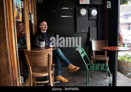 A man takes a coffee break at a cafe in San Francisco, wearing an old Langlitz leather bomber jacket. Stock Photo