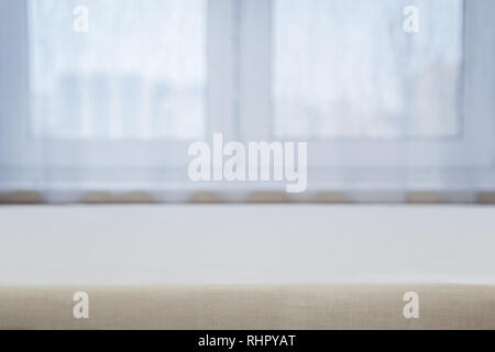 A table with a beige tablecloth against a white window Stock Photo