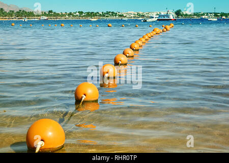 Buoys in the sea. View of the sea from a shore with a long line of orange colored marker buoys floating Stock Photo