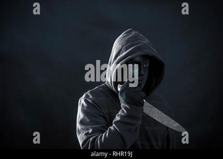 Hooded man with black mask holding knife in the dark Stock Photo