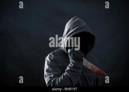 Hooded man with bloody knife in the dark Stock Photo