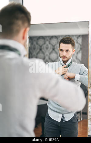 Handsome young man adjusting a tie in front of the mirror. Shopping, fashion, style and people concept Stock Photo