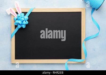 Easter background with funny bunny ears, chalkboard and blue ribbon. Holiday sale mockup with decoration. Stock Photo