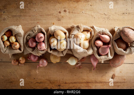 Assortment of onions and potatoes in burlap sack bags, viewed from above on wooden floor. Rustic farm organic harvest concept Stock Photo