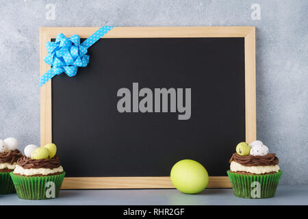 Easter chalkboard background and cupcakes decorated with nest and candy eggs. Copy space. Stock Photo