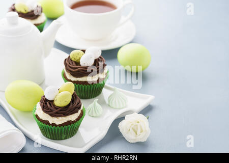 Easter cupcakes decorated with nest, chocolate cream and candy eggs. Holiday treats and tea for breakfast. Stock Photo