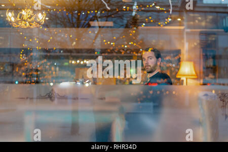 Handsome man with beard in coffee shop with lights reflecting Stock Photo