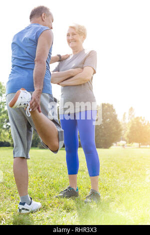Senior man performing quad stretch while taking support of woman in park Stock Photo