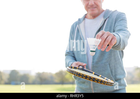 Midsection of senior man with shuttlecock and tennis racket in park Stock Photo