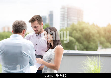 Smiling businesswoman showing document to colleagues at office terrace Stock Photo