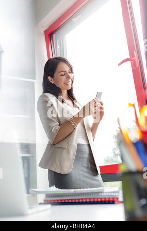 Confident businesswoman texting on smartphone at office Stock Photo