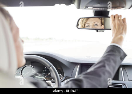 Executive adjusting rear-view mirror driving car during business trip Stock Photo