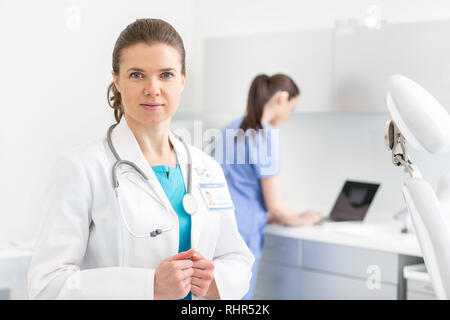 Portrait of smiling doctor standing against nurse using laptop in clinic Stock Photo