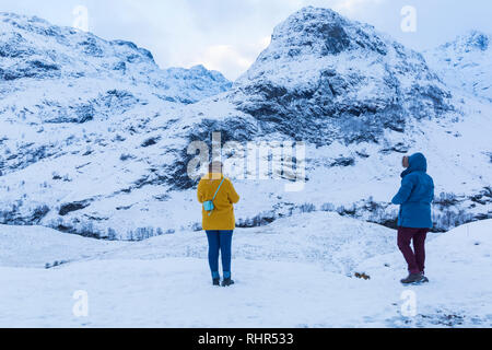 Tourists looking at the snow covered mountains of the Three Sisters from the viewpoint off A82 at Glencoe, Highlands, Scotland in winter