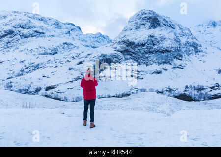 Tourist looking at the snow covered mountains of the Three Sisters from the viewpoint off A82 at Glencoe, Highlands, Scotland in winter