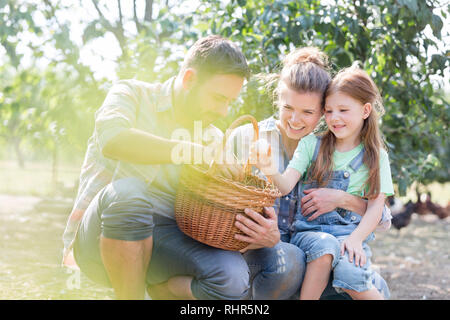 Happy parents and daughter looking at fresh eggs in basket Stock Photo