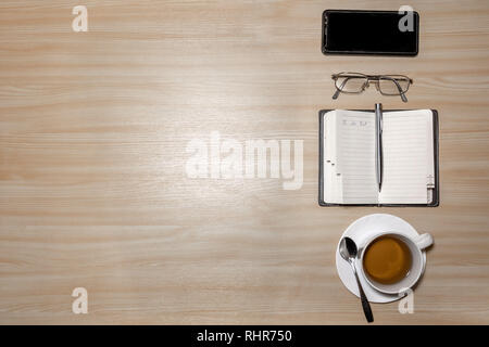 Desk with eyeglasses, notepad, smartphone, pen and a cup of tea on a wooden table. Top view with copy space. Flat lay - image Stock Photo