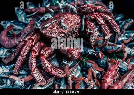 Big hairy boiled crab sits on a heap of dried salted fish on a gift bouquet on the black background. Toned image, close-up Stock Photo