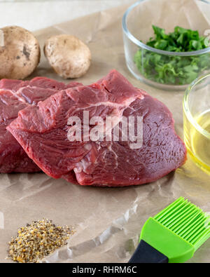 Two steaks being prepared for cooking.  Oil and various spices and herbs.  Mushrooms in background. Stock Photo