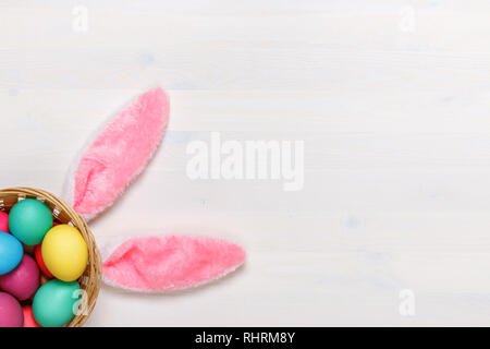 Bunny ears and colorful eggs in a basket on a white background. Easter concept. Copy space Stock Photo