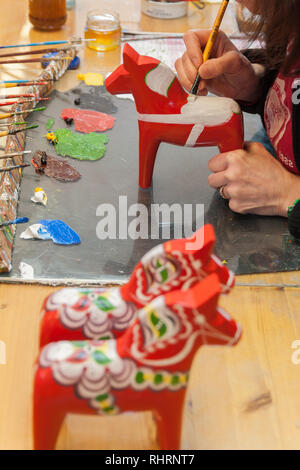 Mora, Sweden. 02/15/2017. Dala Horse factories of Nusnäs. In a workshop of carved Dalecarlian Horse. Employee is painting decoration on wooden horse. Stock Photo