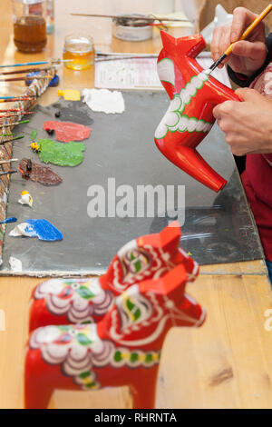 Mora, Sweden. 02/15/2017. Dala Horse factories of Nusnäs. In a workshop of carved Dalecarlian Horse. Employee is painting decoration on wooden horse. Stock Photo