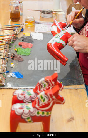 Mora, Sweden. 02/15/2017. Dala Horse factories of Nusnäs. In a workshop of carved Dalecarlian Horse. Employee is painting decoration on wooden horse. Stock Photo