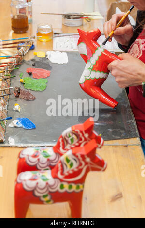 Mora, Sweden. 02/15/2017. Dala Horse factories of Nusnäs. In a workshop of carved Dalecarlian Horse. Employee is painting decoration on wooden horse. Stock Photo