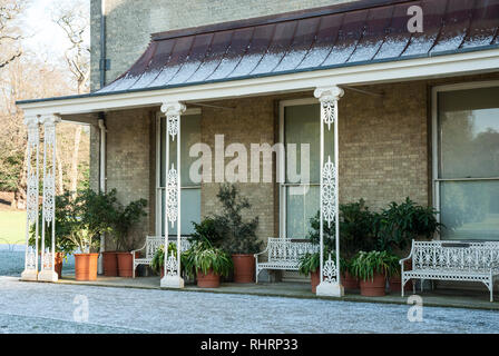 Decorative veranda with ornate wrought iron pillars and benches together with large pot plants on a snowy day in winter at Kenwood House, London Stock Photo