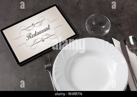 Tablet with stylish restaurant logo and laid table  Stock Photo