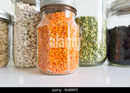 Jars of colorful ingredients artfully arranged in a modern white pantry - orange, green, black and white beans, peas, lentils and more Stock Photo