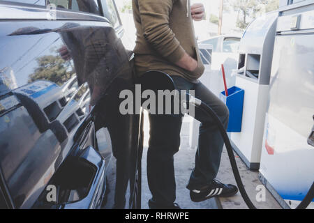 Man pumping fuel into his vehicle while watching the price display at service station in Los Angeles, California, USA Stock Photo