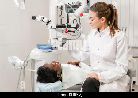 Female dentist advanced user, dental tools. Looking into the lens of a microscope while examining his patients teeth. in dental clinic office Stock Photo