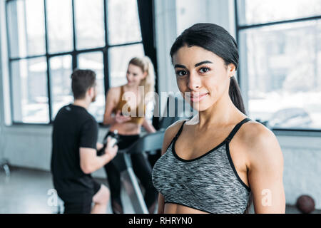 beautiful african american sportswoman smiling at camera, young friends training behind in gym Stock Photo