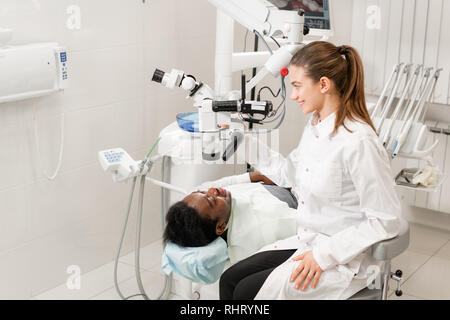Female dentist advanced user, dental tools. Looking into the lens of a microscope while examining his patients teeth. in dental clinic office Stock Photo