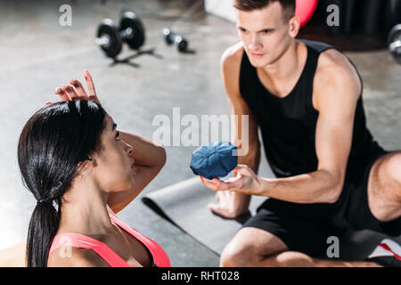 sportsman giving ice pack to young african american woman suffering from injury in gym Stock Photo