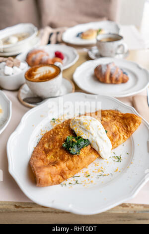 Breakfast. Frittata - italian omelet. Omelette with tomatoes, avocado, spinach and soft cheese. Croissants, coffee and other dishes on the table in Stock Photo