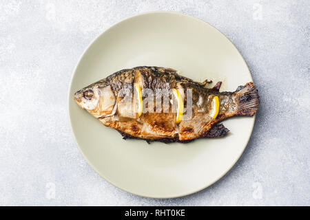 Baked fish carp with lemon greens on a plate Stock Photo
